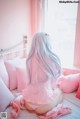 A woman sitting on a bed with pink pillows and a stuffed animal.