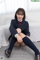 A woman in a school uniform sitting on a bed.