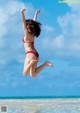 A woman in a red bikini jumping in the air on the beach.