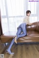 A woman sitting on a brown couch wearing blue tights.