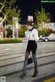 A woman in a white shirt and black skirt crossing the street.