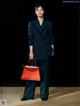 A woman in a black suit holding a red handbag.