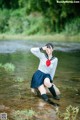 A woman in a school uniform sitting on a rock in the water.