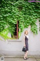 A woman standing in front of a wall covered in ivy.