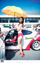 A woman holding an umbrella standing next to a race car.