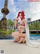 A woman in a bikini sitting on the ground next to a pool.