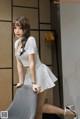 A woman in a white dress leaning against a wall.