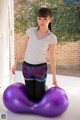 A young woman sitting on a purple exercise ball.