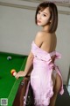 A woman in a pink dress standing next to a pool table.