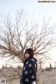 A woman standing in front of a bare tree in the desert.