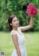 A woman in a white dress holding a pink flower.