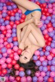 A woman laying in a ball pit filled with pink and purple balls.