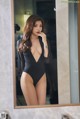 A woman in a black bodysuit standing in front of a mirror.